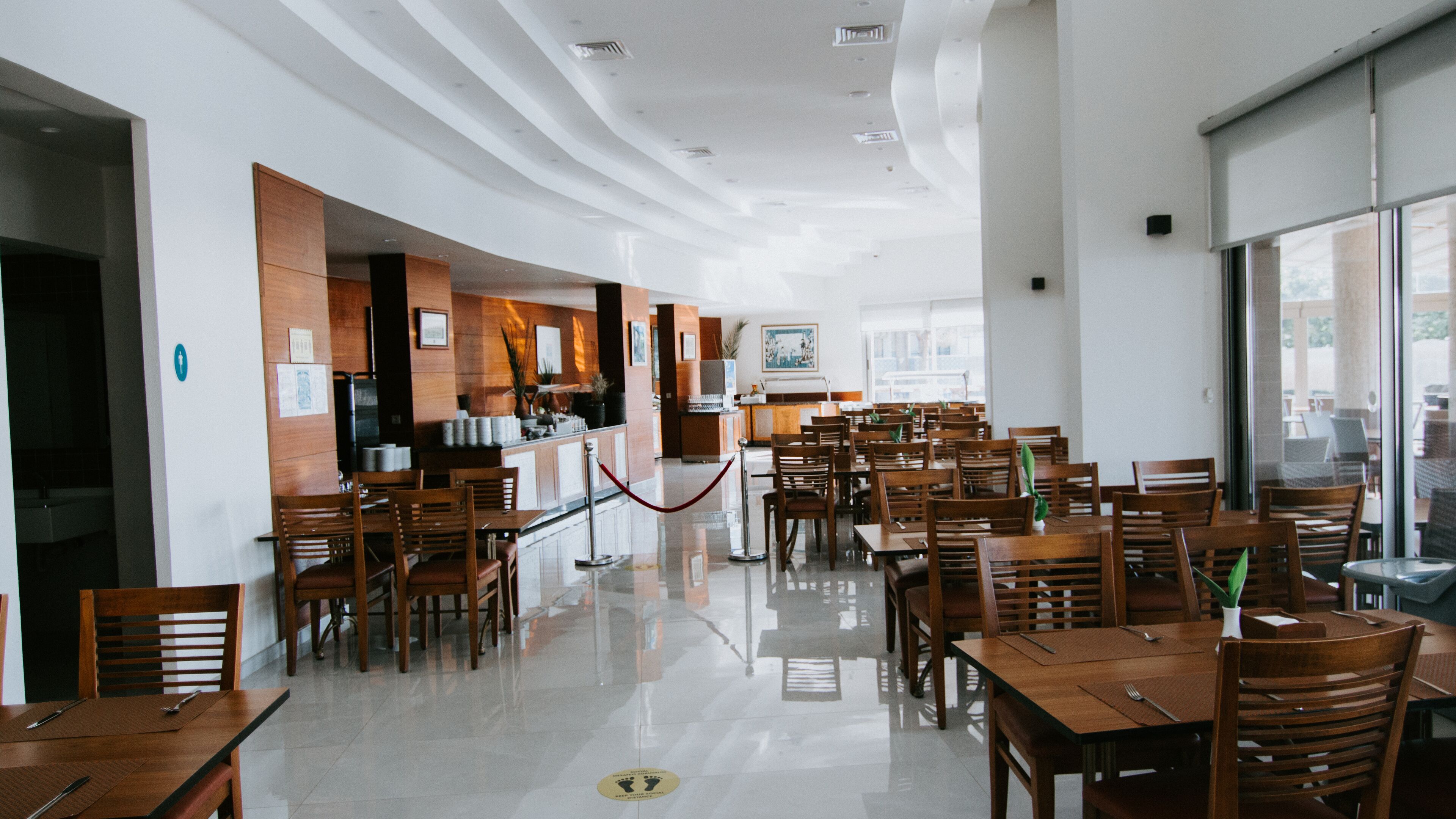 A spacious restaurant with a long counter, wooden chairs, and tables.
