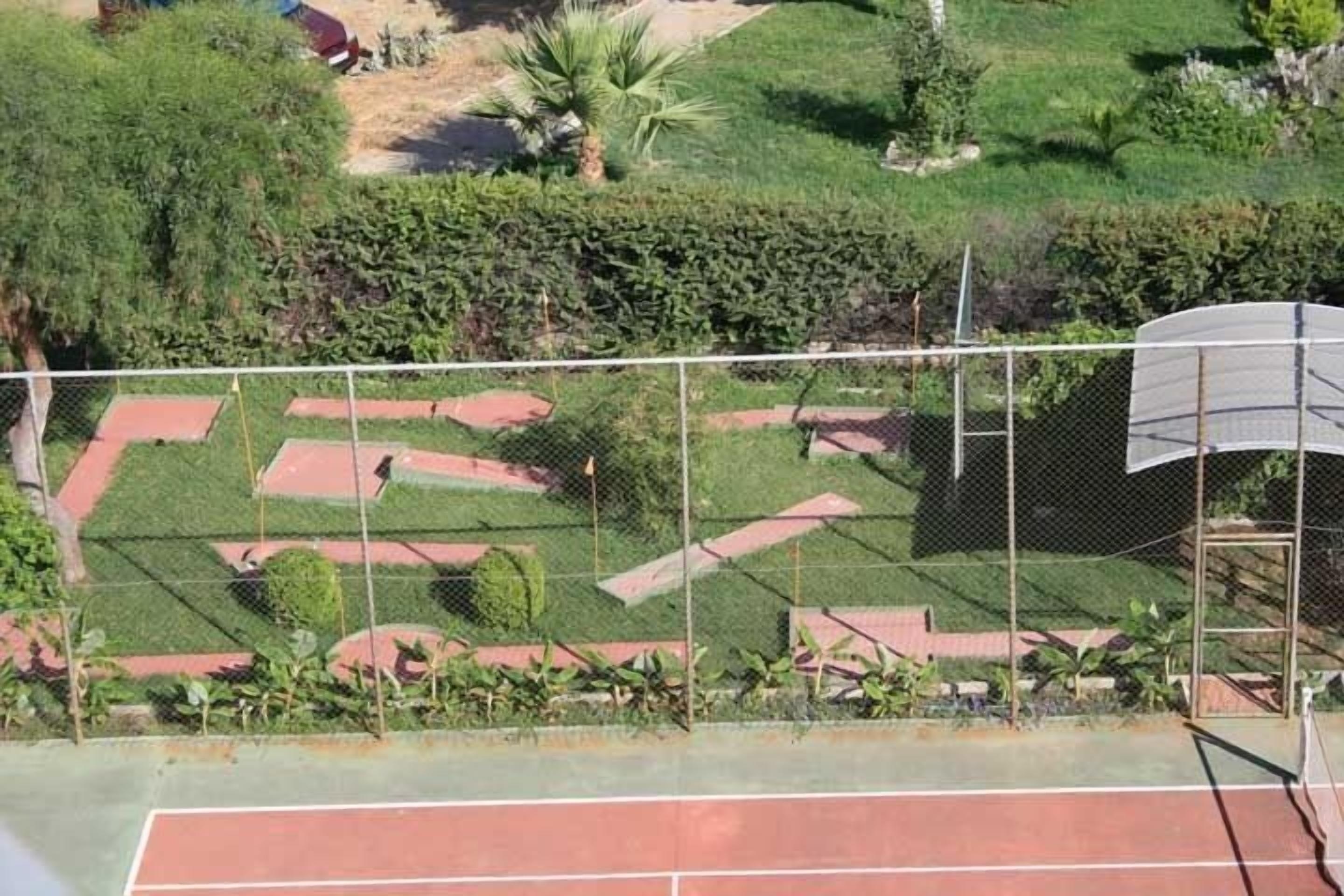 Una cancha de tenis con un jardín alrededor y una valla.