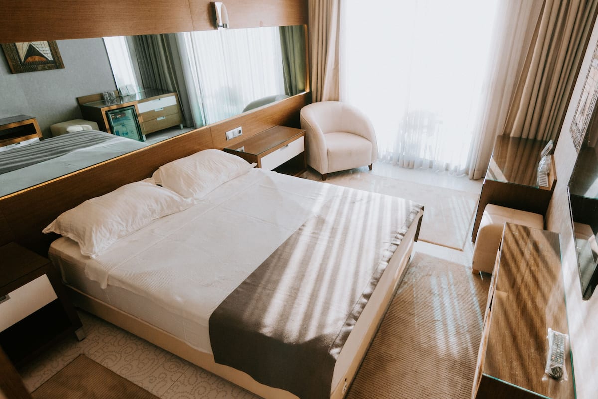 A hotel room with a large bed, bedside tables, a chair, a desk, a TV, and a window with curtains.