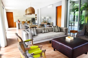 Una sala moderna con un sofá gris, sillas de madera, una mesa de centro y un área de comedor al fondo.