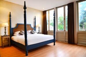A four-poster bed with a dark wooden frame and white bedding, positioned in a room with large windows and a view of greenery outside. - Jabu Beach Villa (Canggu)