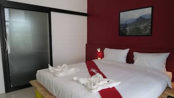 A hotel room with a bed, a red accent wall, a framed picture, and a bench.