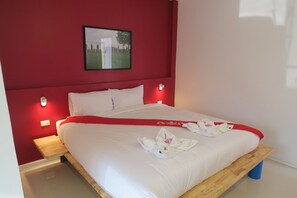 A neatly made bed with white linens and a red accent, a wooden nightstand, and a wall-mounted picture. - Montha Hotel (Chiang Mai)