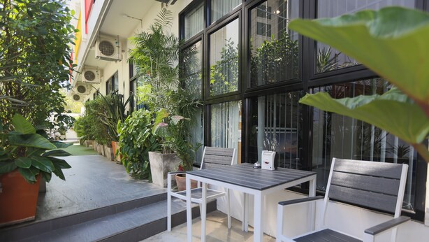 A patio area with a table and two chairs, surrounded by potted plants and a building with large windows. - Montha Hotel (Chiang Mai)