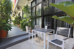 A patio area with a table and two chairs, surrounded by potted plants and a building with large windows. - Montha Hotel (Chiang Mai)