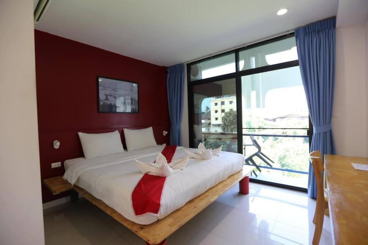 A hotel room with a bed, a window with curtains, a balcony, and a view of buildings.