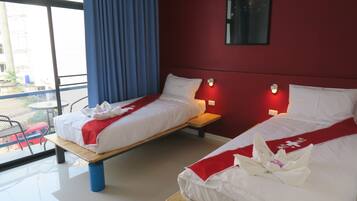 Habitación de hotel con dos camas, cada una con ropa blanca y detalles rojos, un balcón con mesa y sillas, y una pared roja con un espejo.