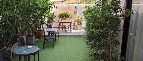 Un patio con césped artificial, una mesa y sillas, y plantas en macetas.