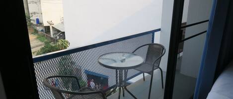 A balcony with a round table and two chairs, a bed, and a view of the street.
