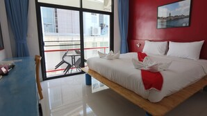 A hotel room with a bed, a desk, and a balcony with a view of buildings. - Montha Hotel (Chiang Mai)