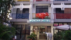 A hotel with a distinctive red cow sculpture in front, a sign reading "MONTHA HOTEL," and a staircase leading to the entrance. - Montha Hotel (Chiang Mai)