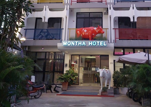 A hotel with a distinctive red cow sculpture in front, a sign reading "MONTHA HOTEL," and a staircase leading to the entrance. - Montha Hotel (Chiang Mai)