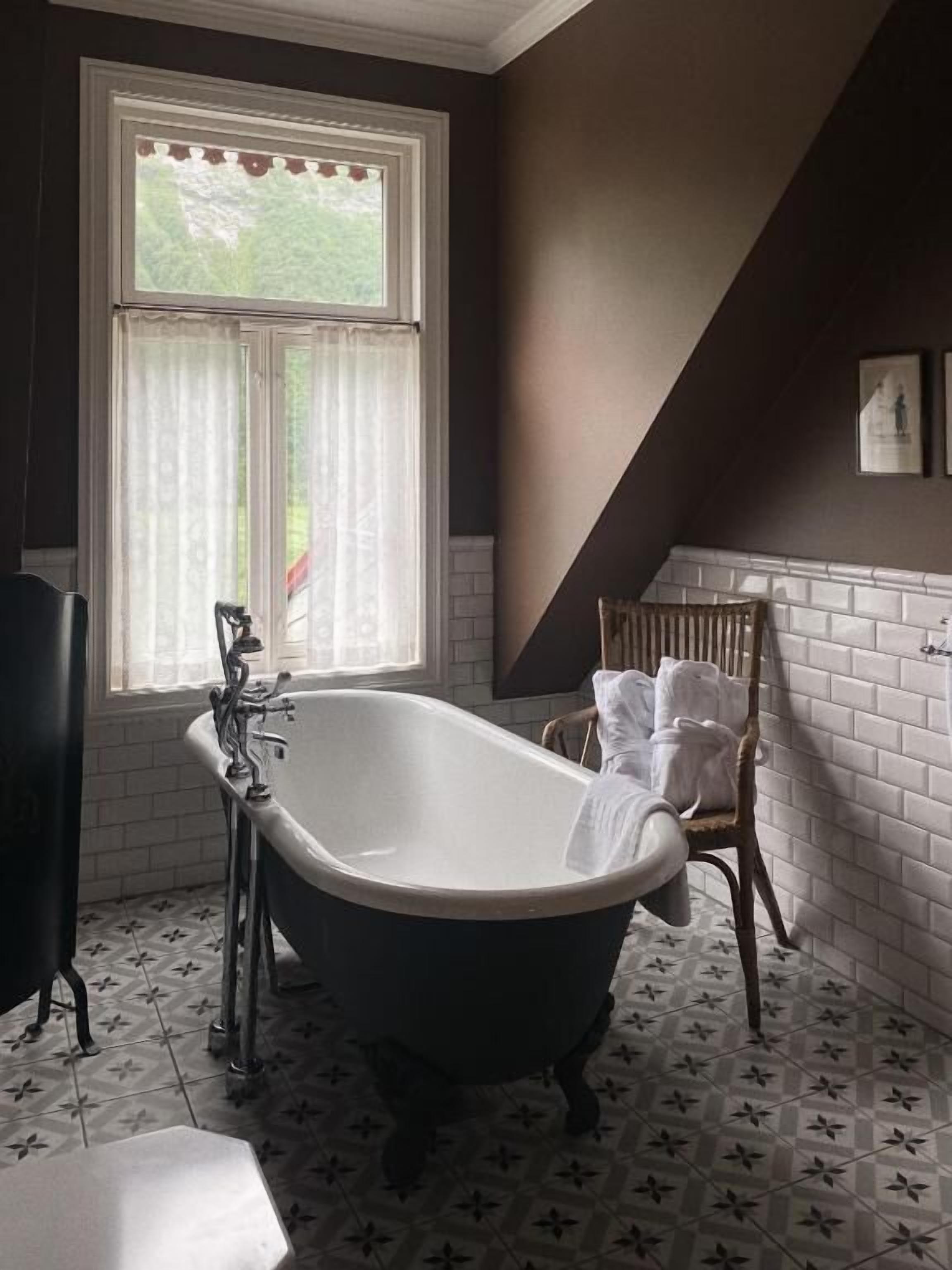 A bathroom with a freestanding bathtub, a window with curtains, and a radiator.