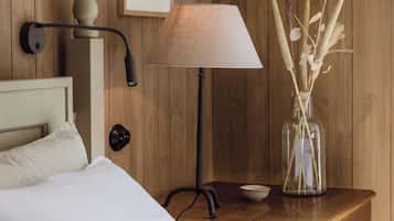 A wooden-paneled room with a bed, a nightstand with a lamp, a framed picture, and a vase with dried plants.