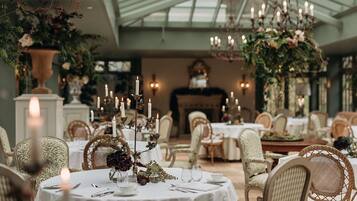A formal dining room with round tables, white tablecloths, and candlelit centerpieces.