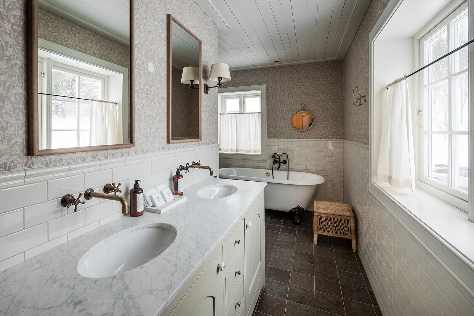 A bathroom with a double sink, a bathtub, a mirror, and a window.