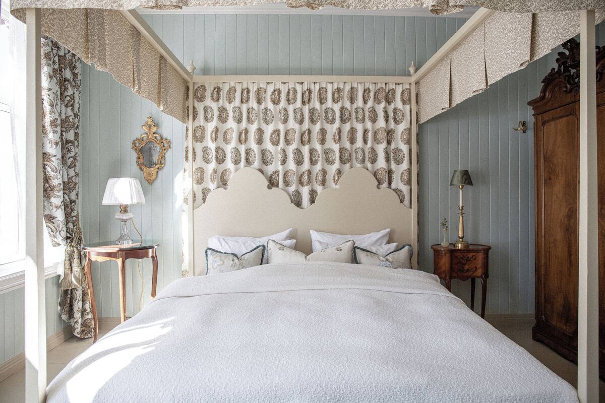 A bedroom with a bed, a nightstand, a lamp, a mirror, and a wardrobe.