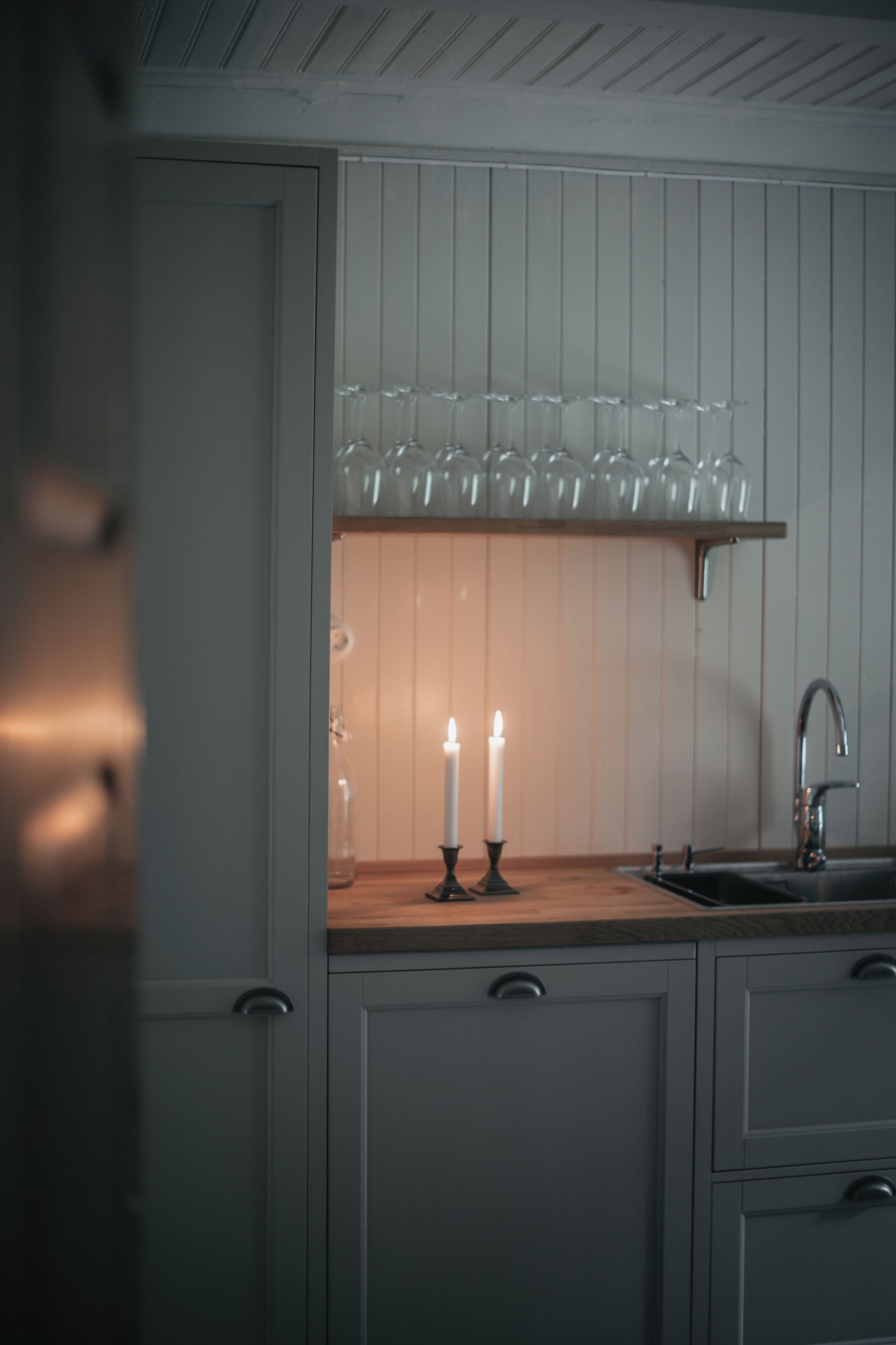 A kitchen with a wooden countertop, a built-in shelf with glassware, a sink, and two lit candles.
