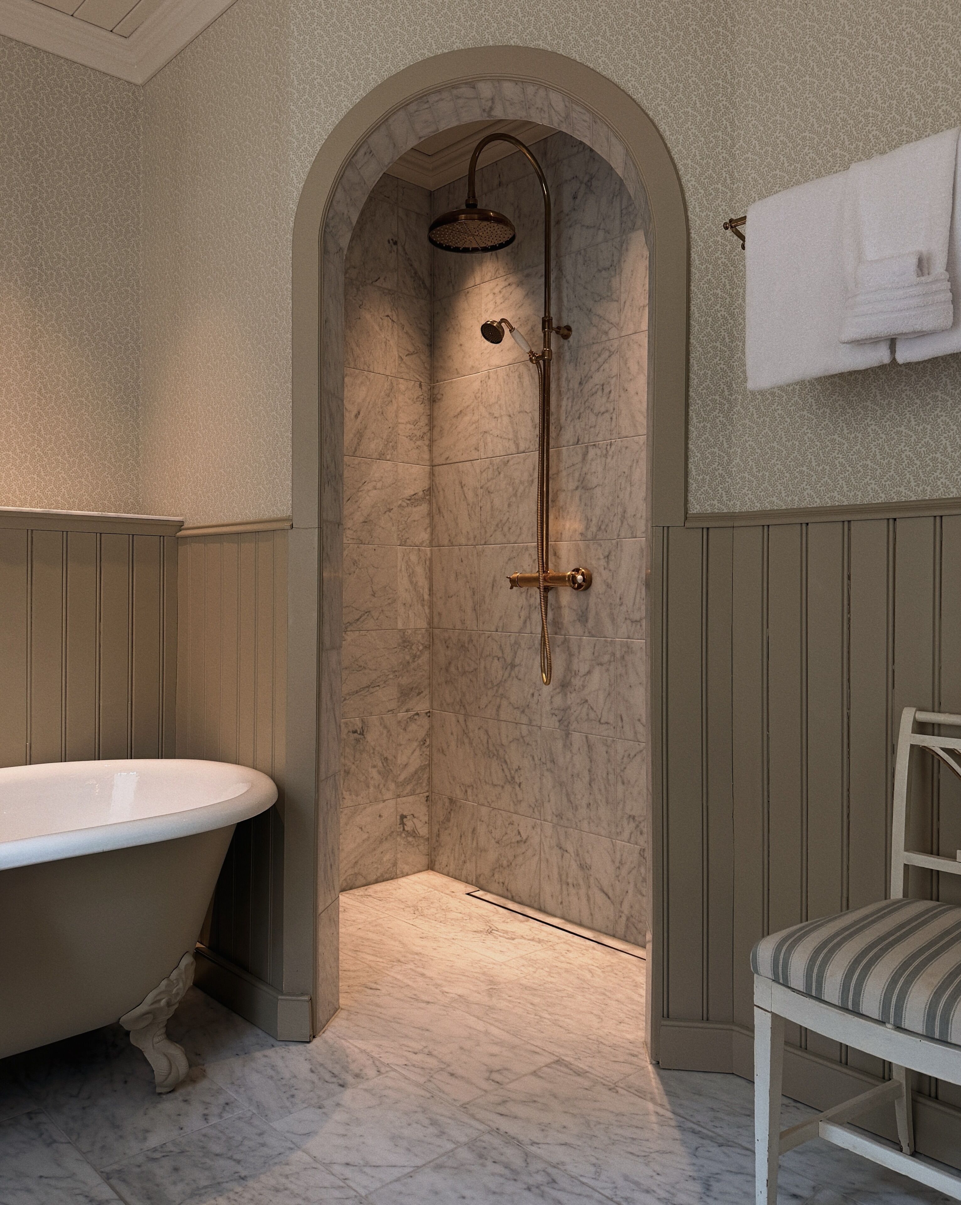 Een badkamer met een vrijstaand bad, een douche met een handdouche en een stoel.