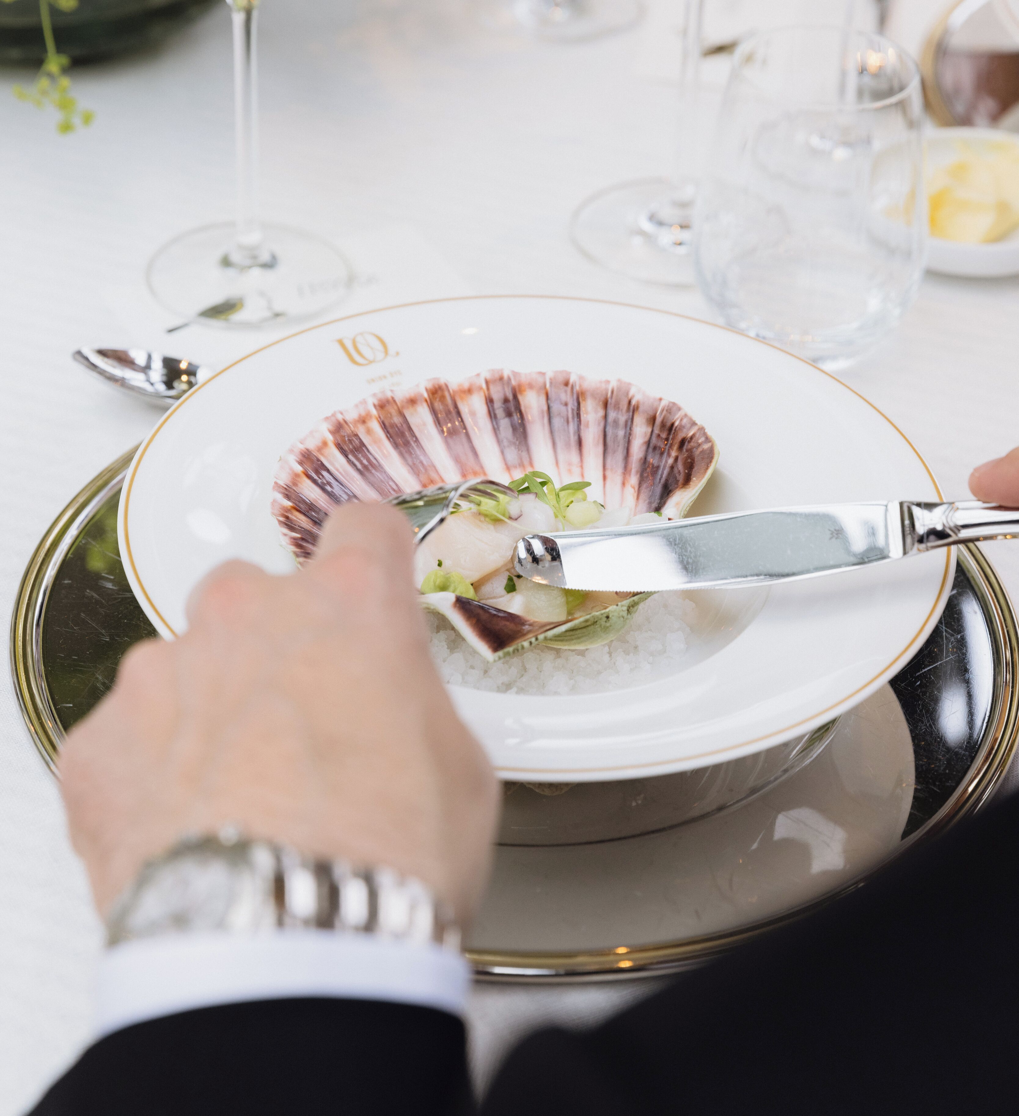 A person using a knife to cut food from a shell-shaped plate on a tray.