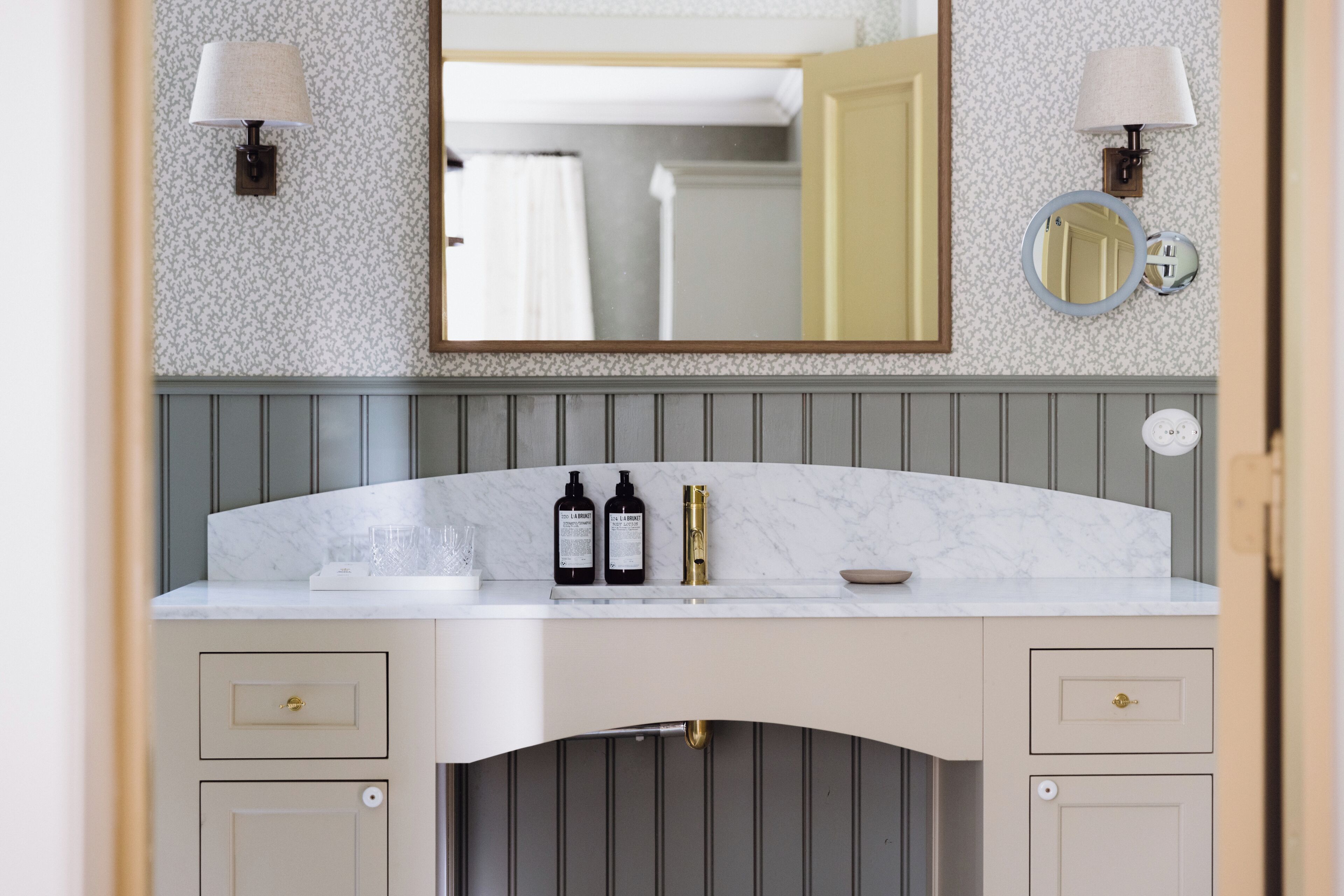 A bathroom with a marble vanity, two wall-mounted lamps, a mirror, and a towel rack.