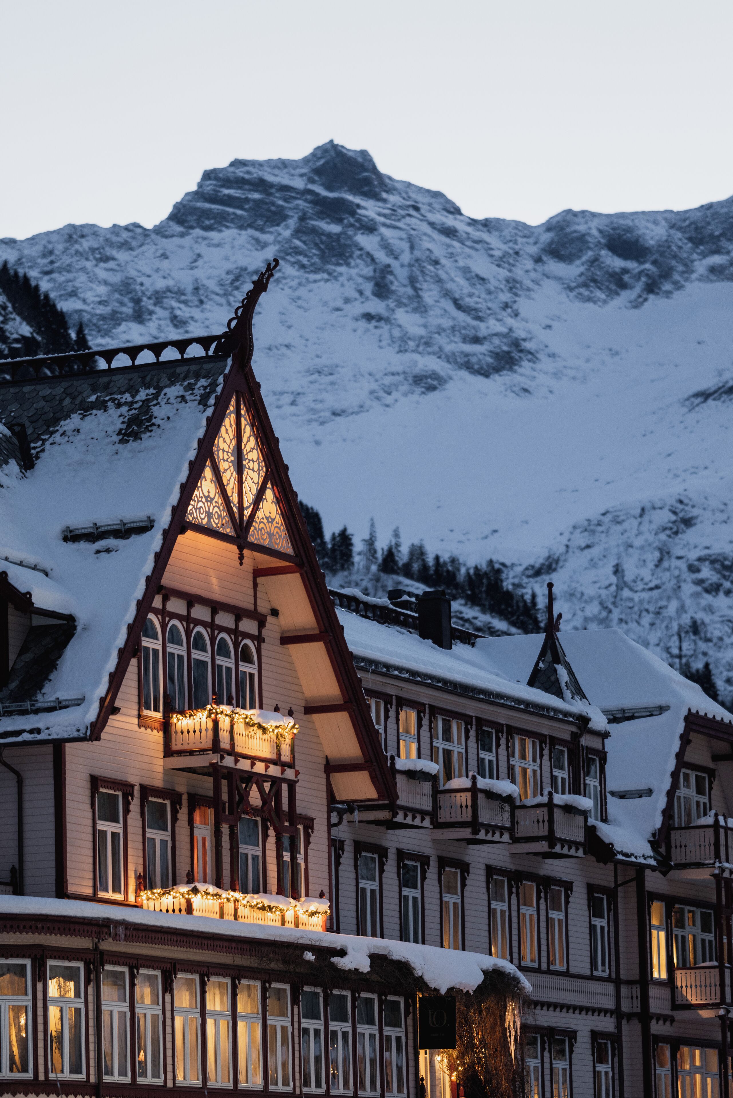 A traditional chalet with multiple balconies and a steeply pitched roof, surrounded by snow-covered mountains.