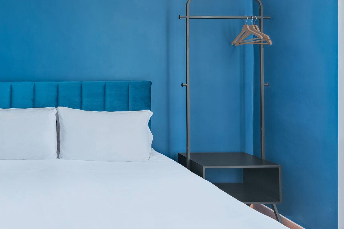 A room with a bed, a blue wall, and a metal rack with clothes.