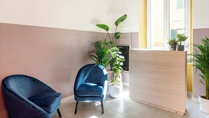 A modern room with a blue chair, a wooden reception desk, and potted plants. - Hotel Infinito (Rome)