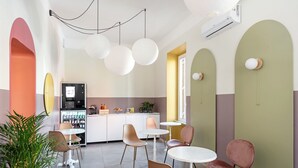 A modern cafe with round tables and chairs, a kitchen area, and a large window providing natural light. - Hotel Infinito (Rome)