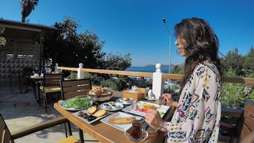 A dining area with a table set for a meal, outdoor seating, and a view of the sea.