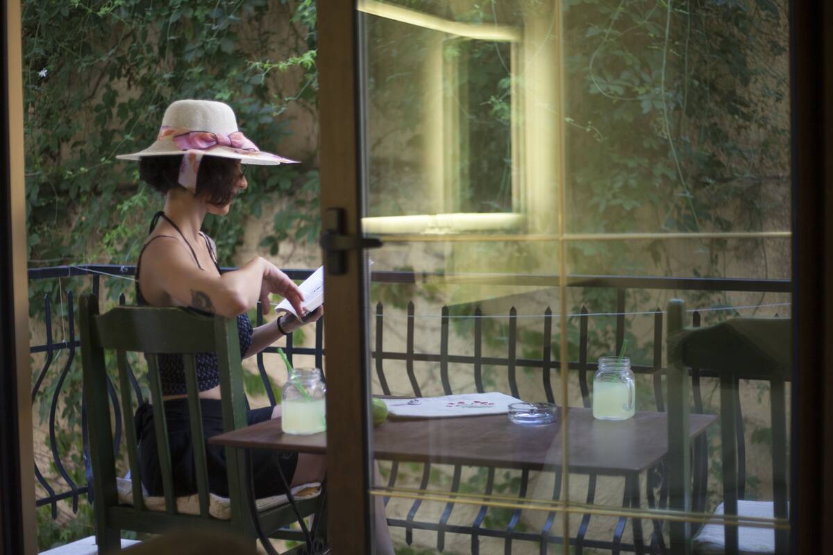 Una persona sentada en una mesa, con una bebida y un menú, al aire libre con vista a follaje.