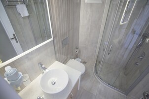 Un baño moderno con ducha de vidrio, lavamanos blanco y retrete.