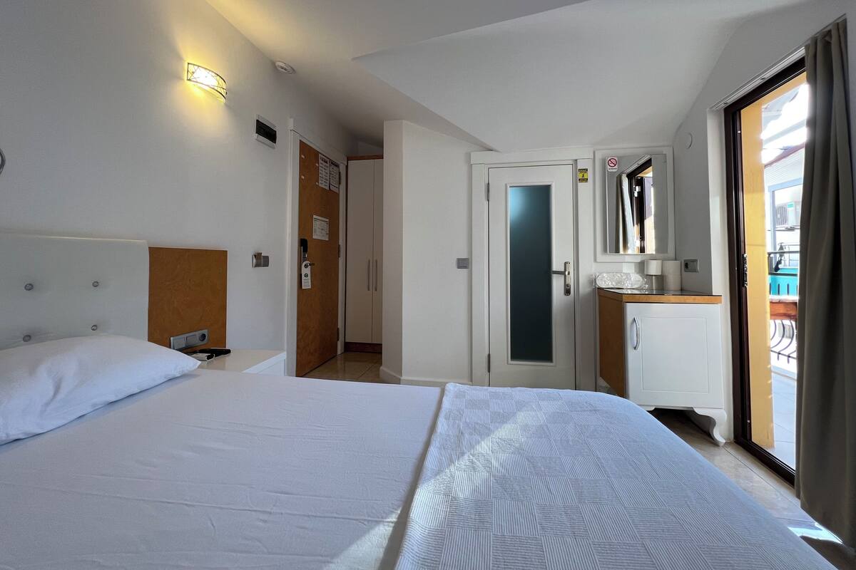 Habitación de hotel con cama, escritorio, armario y puerta corrediza a un balcón.