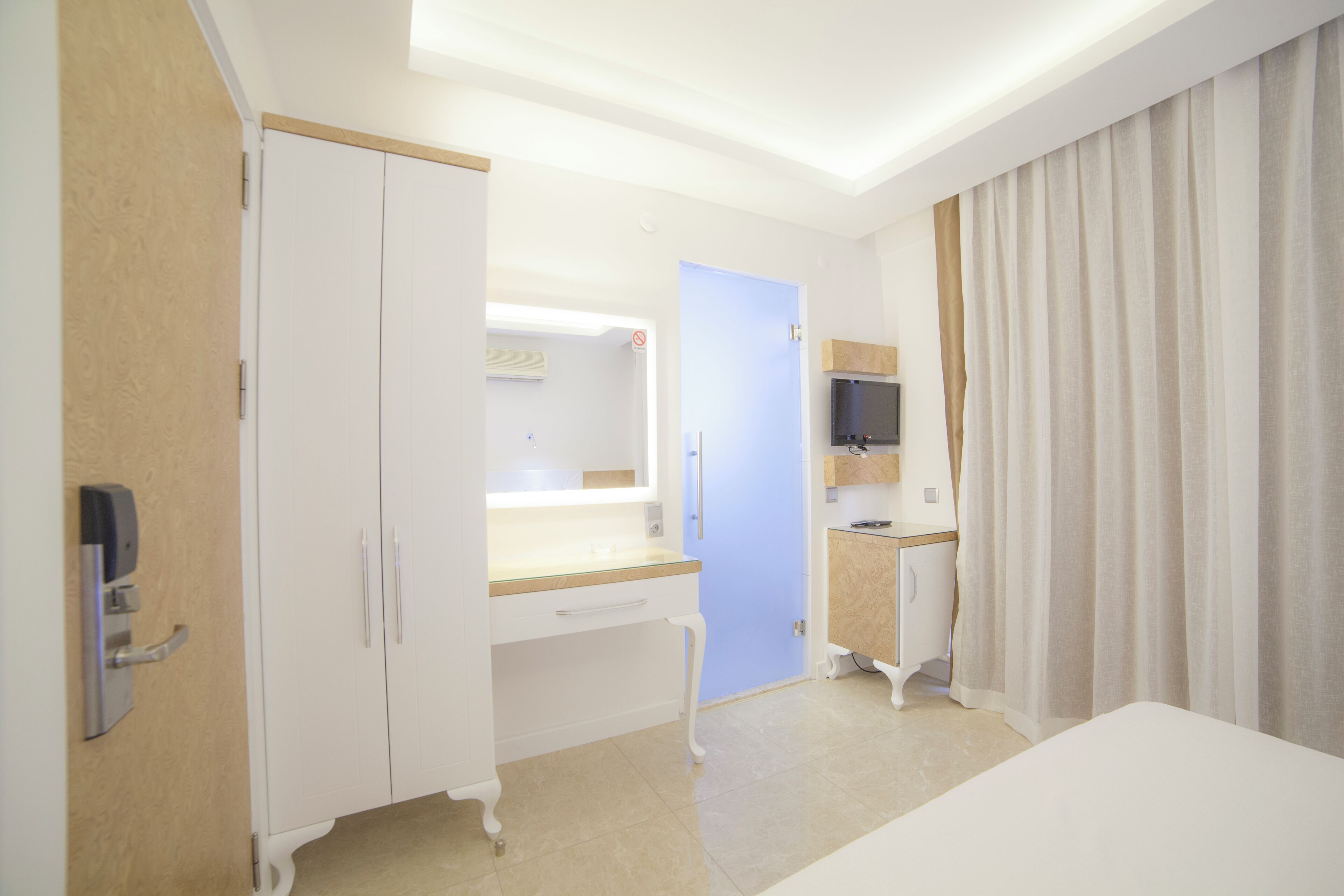 A hotel room with a bed, a desk, a mirror, a television, and a wardrobe.