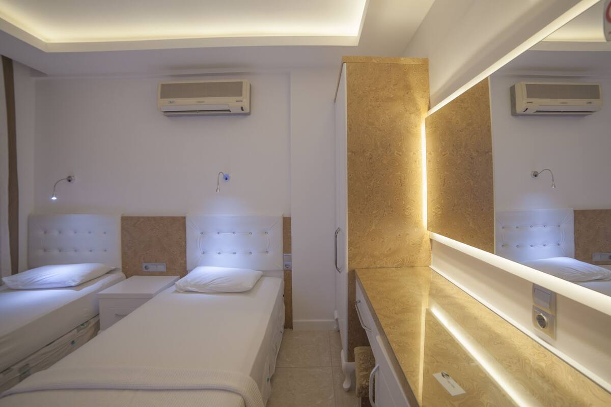 Habitación de hotel con dos camas, un espejo grande y dos unidades de aire acondicionado fijadas a la pared.