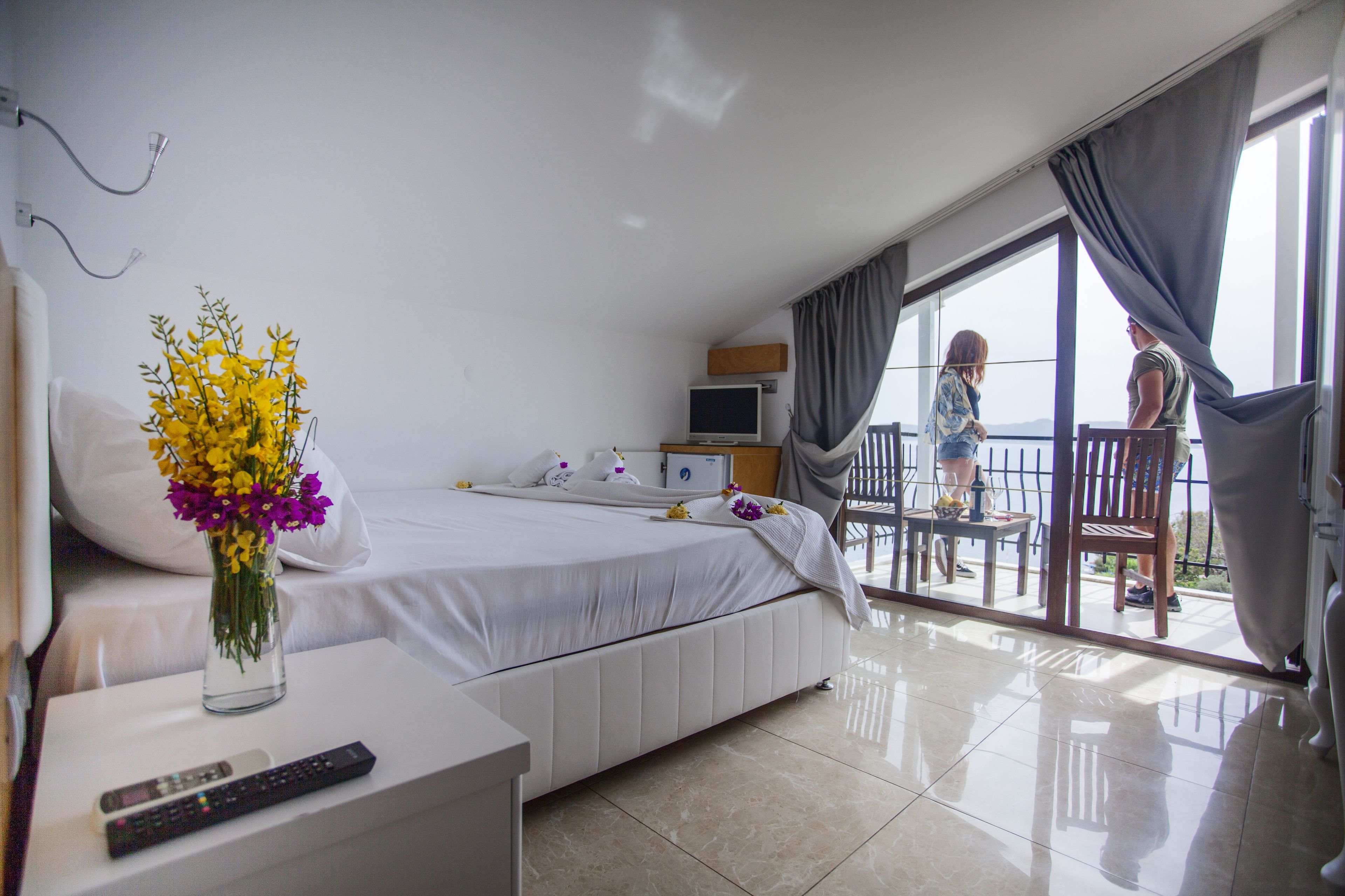 Une chambre d’hôtel comprenant un lit, une table de chevet avec une télécommande, une télévision et un balcon avec une table et des chaises.