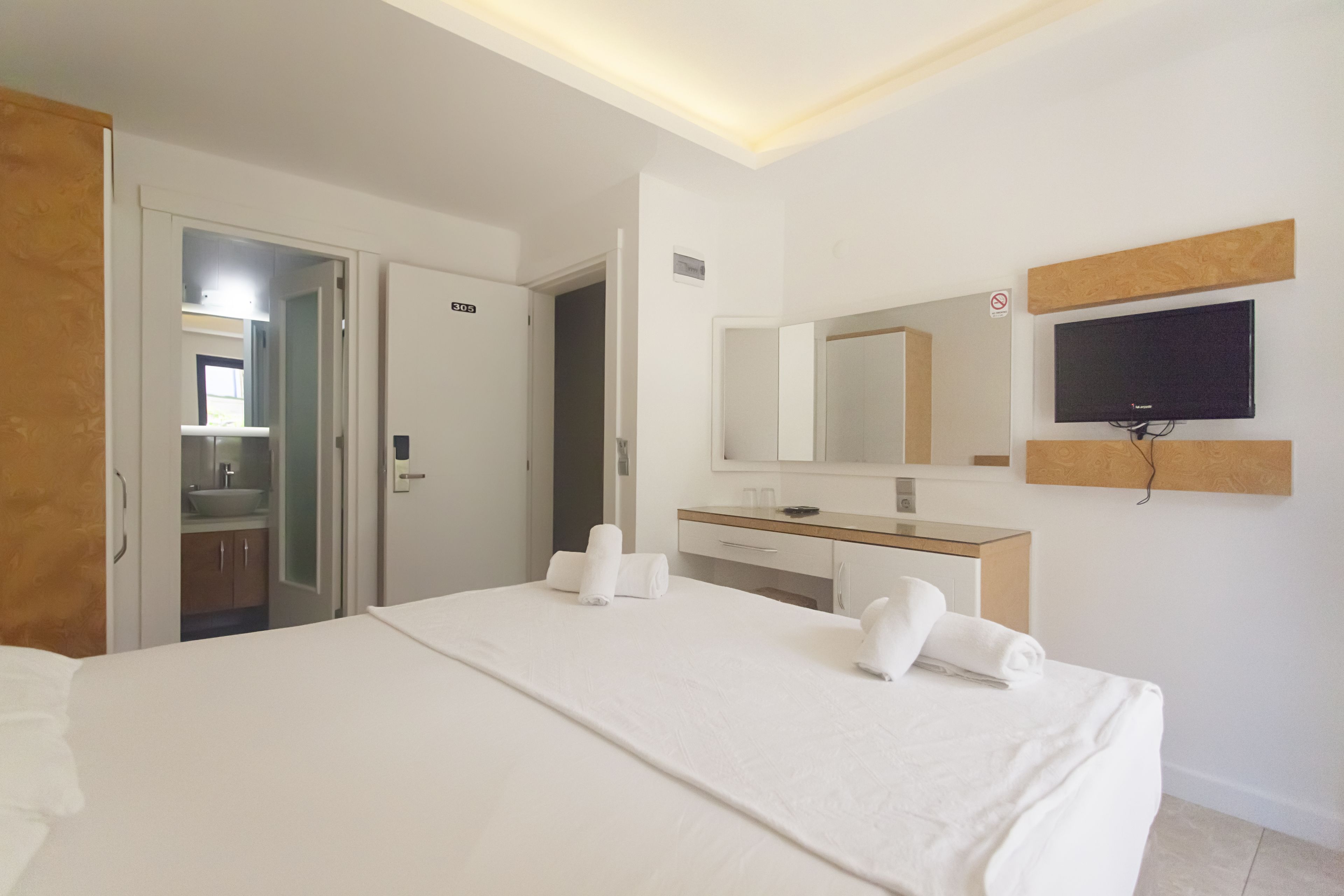 A hotel room with a bed, a TV mounted on the wall, a bathroom with a sink, and a door leading to another room.