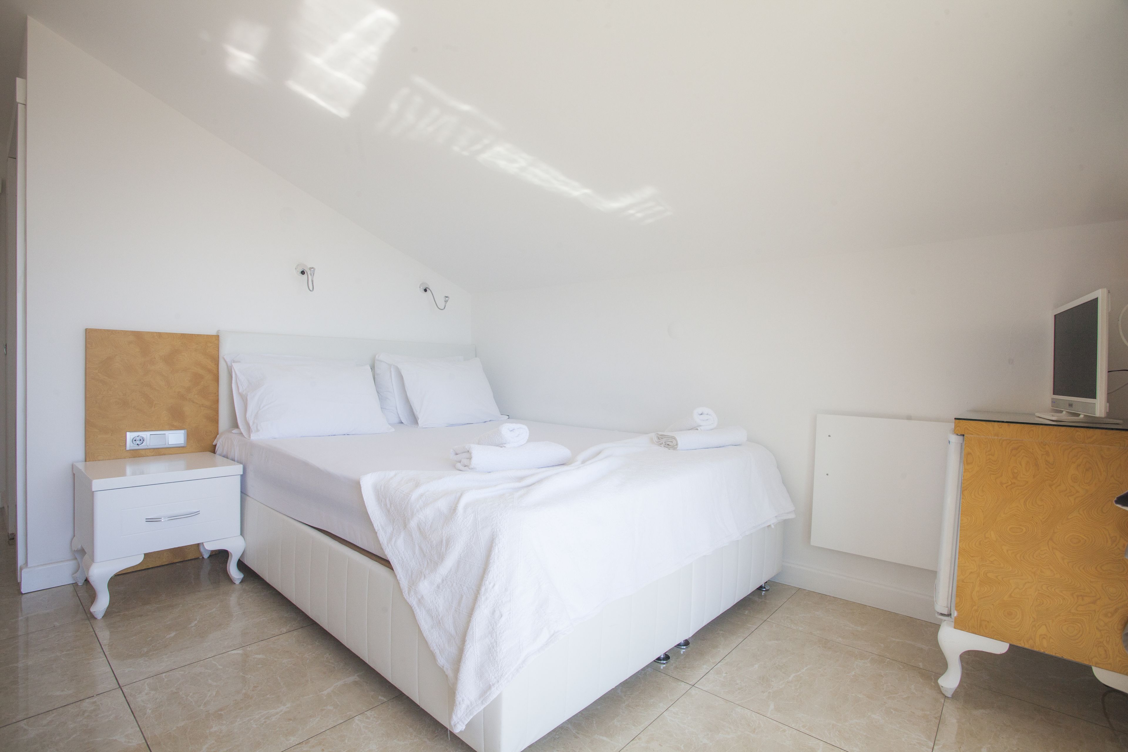 A bedroom with a bed, a nightstand, a wooden dresser, and a wall-mounted TV.