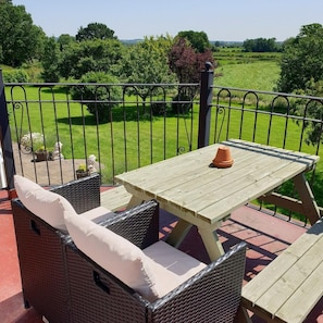 A wooden table and wicker chairs on a balcony with a metal railing, overlooking a green landscape. - The Moorhead Bed & Breakfast (Shrewsbury)