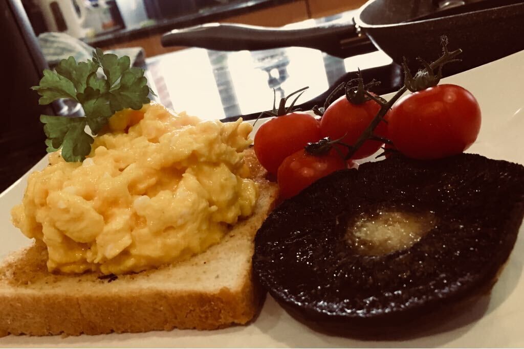Des œufs brouillés sur des toasts, une tranche de boudin noir et des tomates cerises dans une assiette.