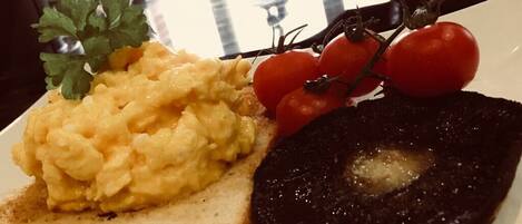 Des œufs brouillés sur des toasts, une tranche de boudin noir et des tomates cerises dans une assiette.