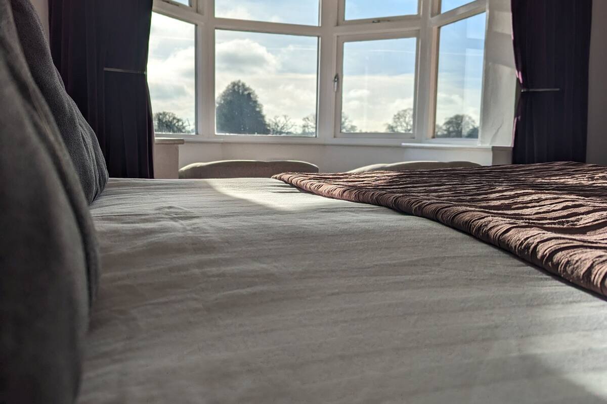 A bedroom with a large bed, a view of the sky through a window, and a ceiling light fixture.