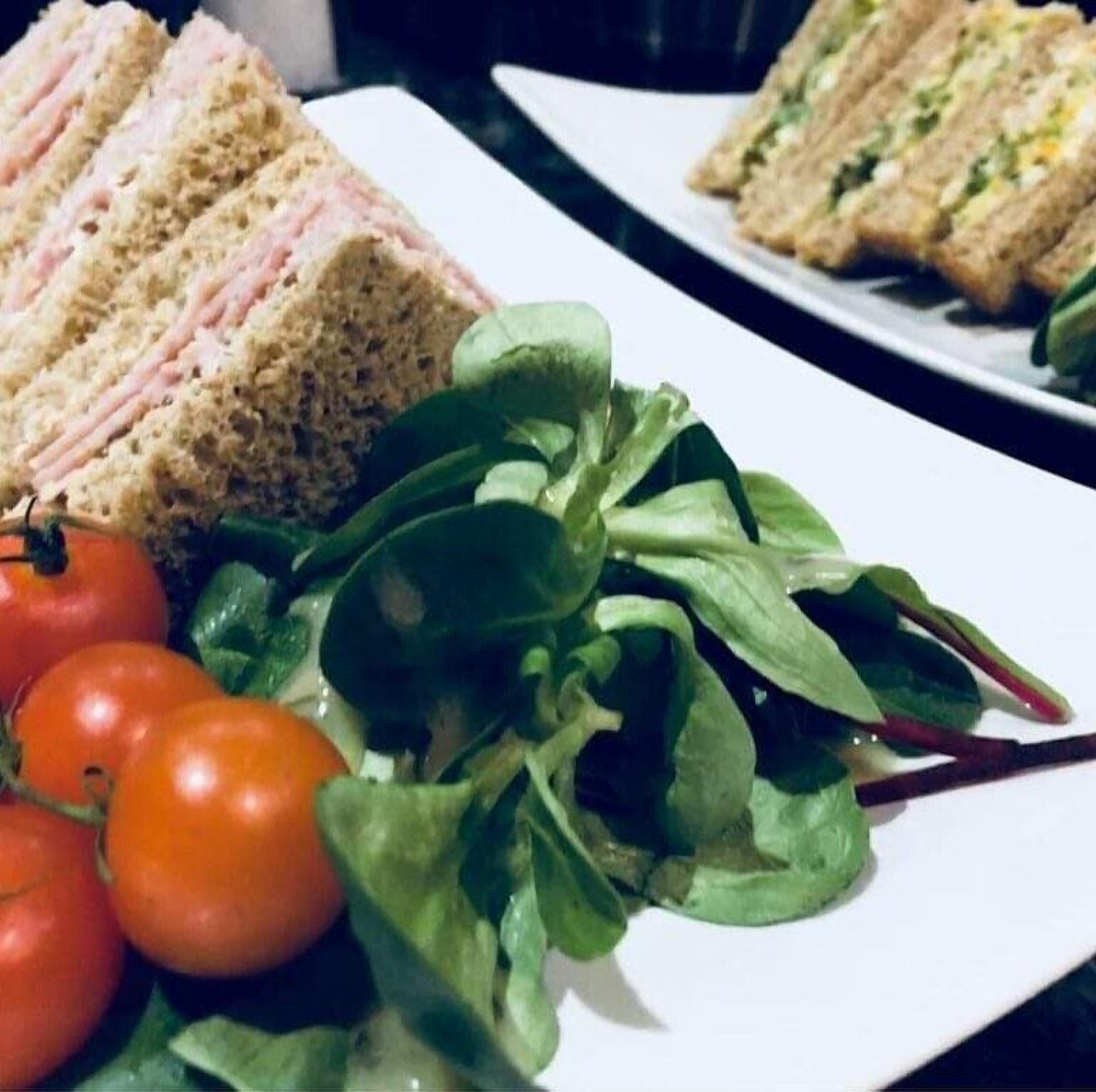 A plate with a layered sandwich, cherry tomatoes, and leafy greens.