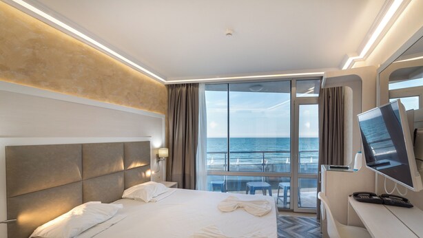 Ett hotellrum med en stor säng, ett skrivbord med en dator och utsikt över havet.