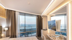Ett hotellrum med en stor säng, ett skrivbord med en dator, en stol, en tv och utsikt över havet.