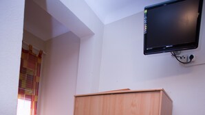 Una habitación con un armario de madera, un escritorio y un televisor de pared.