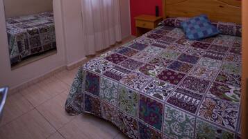 Un dormitori amb una paret vermella, un llit de fusta, un ventilador de sostre, una finestra amb cortines i un mirall a la pared.