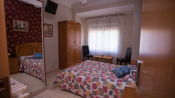 Un dormitorio con cama, escritorio, silla, armario y televisor.