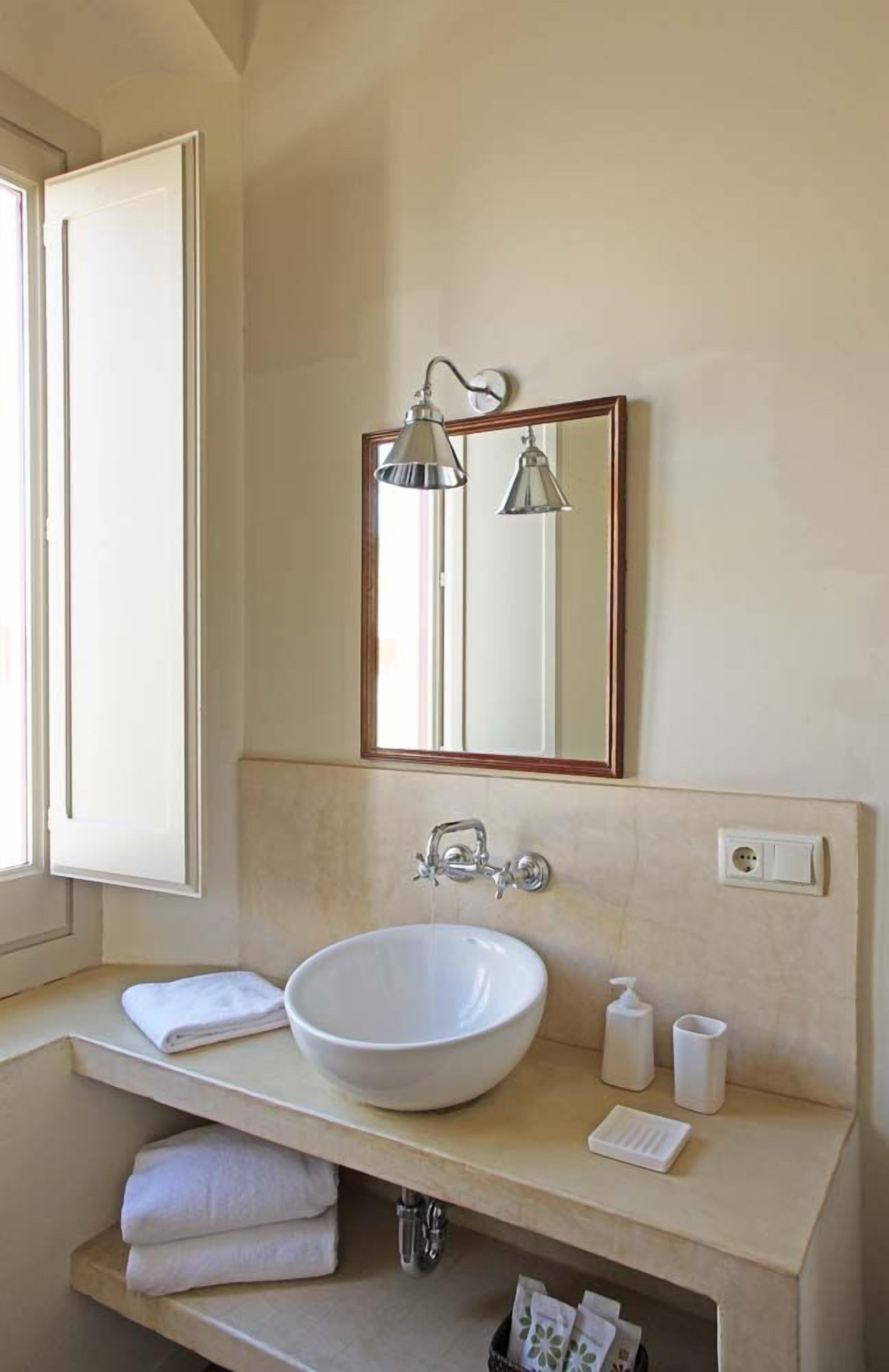 A bathroom with a large white sink, a mirror, a towel rack, and a window.