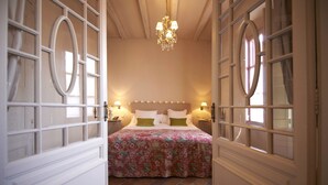 Un dormitorio con una cama grande, dos mesitas de noche, una araña y suelo de ladrillo.